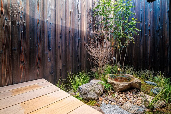 A wooden deck adjacent to a wooden fence with a small tree and rocks.