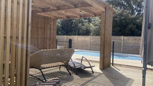 A wooden deck with a pool, two wicker chairs, and a pergola. - Charming Villa Near Beach with Heated Pool, Wi-Fi, Billiards, and Garage (La Tranche-sur-Mer)