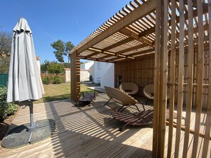 Une pergola en bois avec un espace salon abrité, une table et un parasol.
