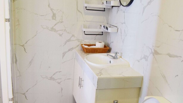 A bathroom with a marble wall, a sink, a mirror, and a toilet. - A's Place (Valencia)