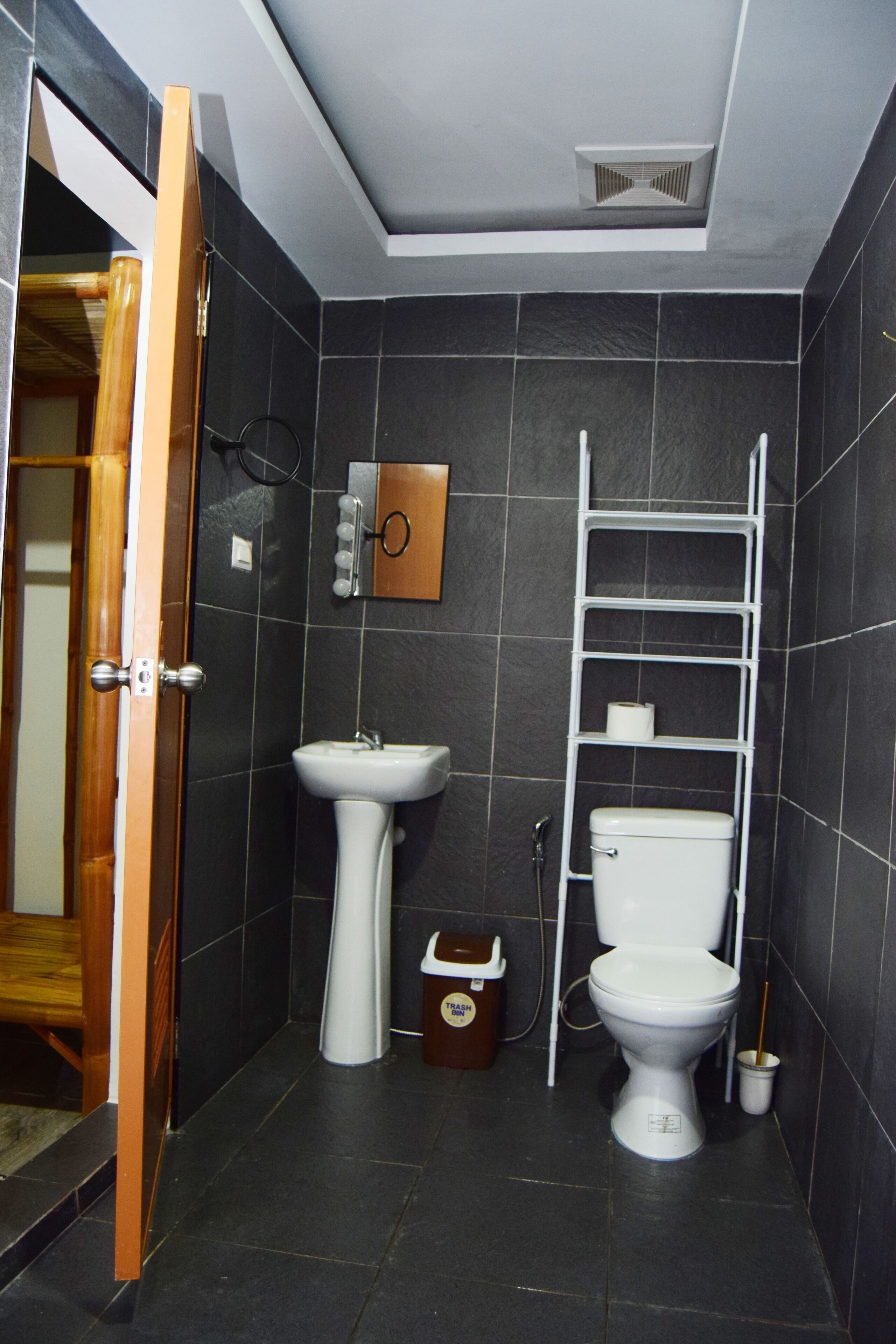 A compact bathroom with a pedestal sink, toilet, and a white shelf unit.