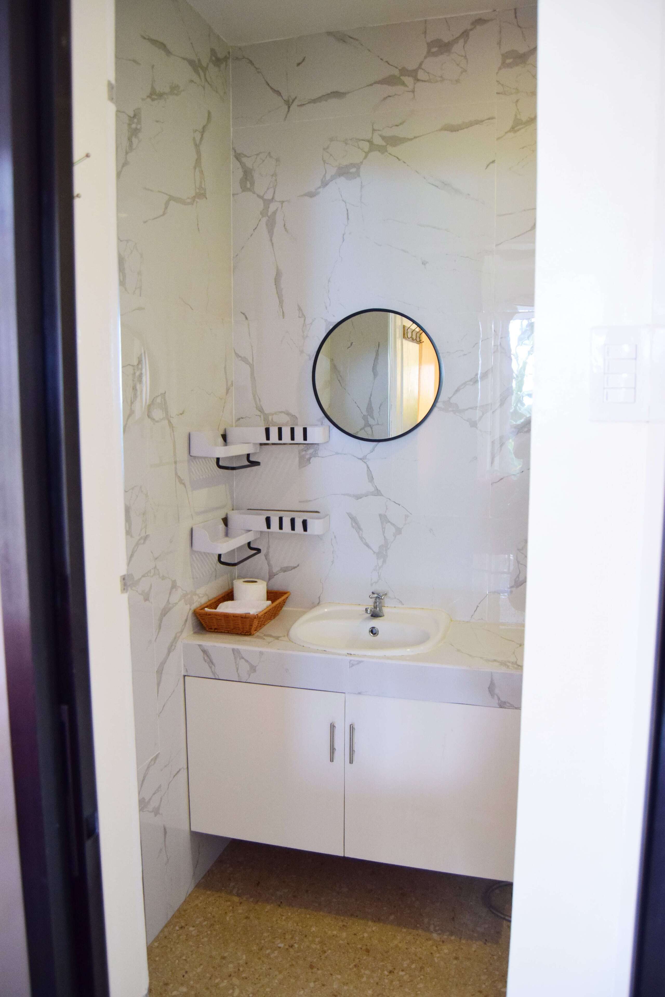 Un baño con pared de mármol, un espejo redondo, un lavabo blanco y un mueble.
