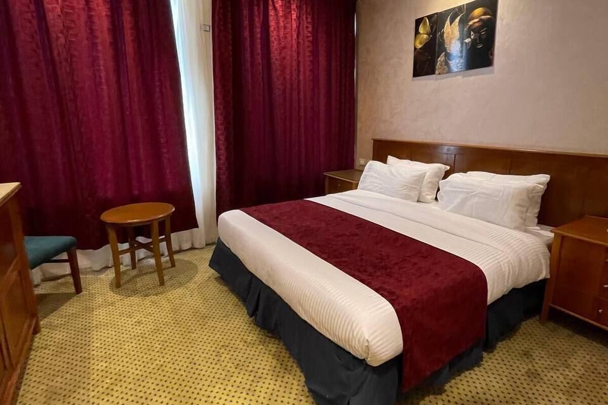 A hotel room with a large bed, a small table, a chair, and a painting on the wall.