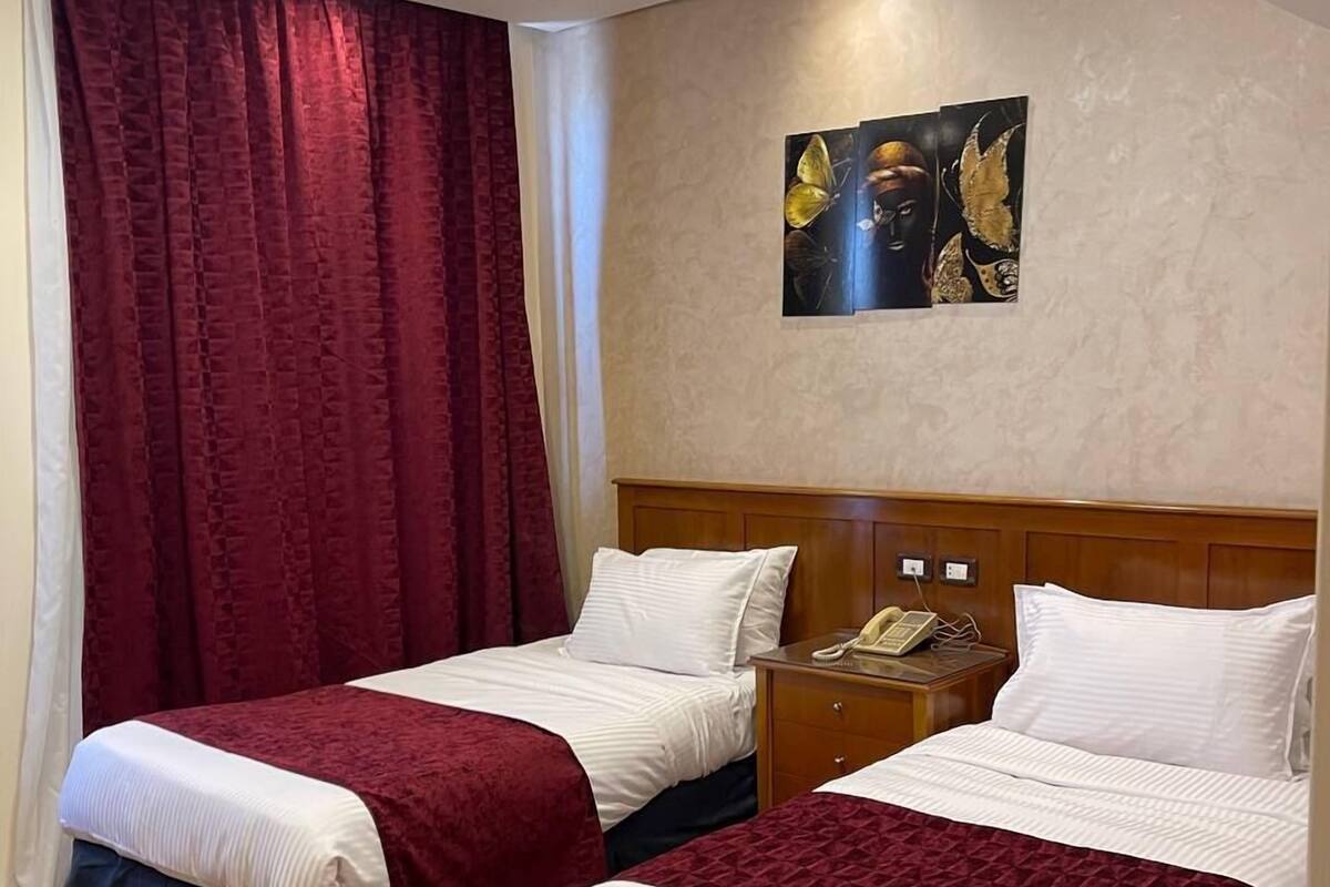A hotel room with two beds, a nightstand with a phone, and a painting on the wall.