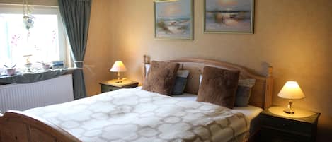 A bedroom with a wooden bed, two bedside tables with lamps, a window with curtains, and two framed pictures on the wall.