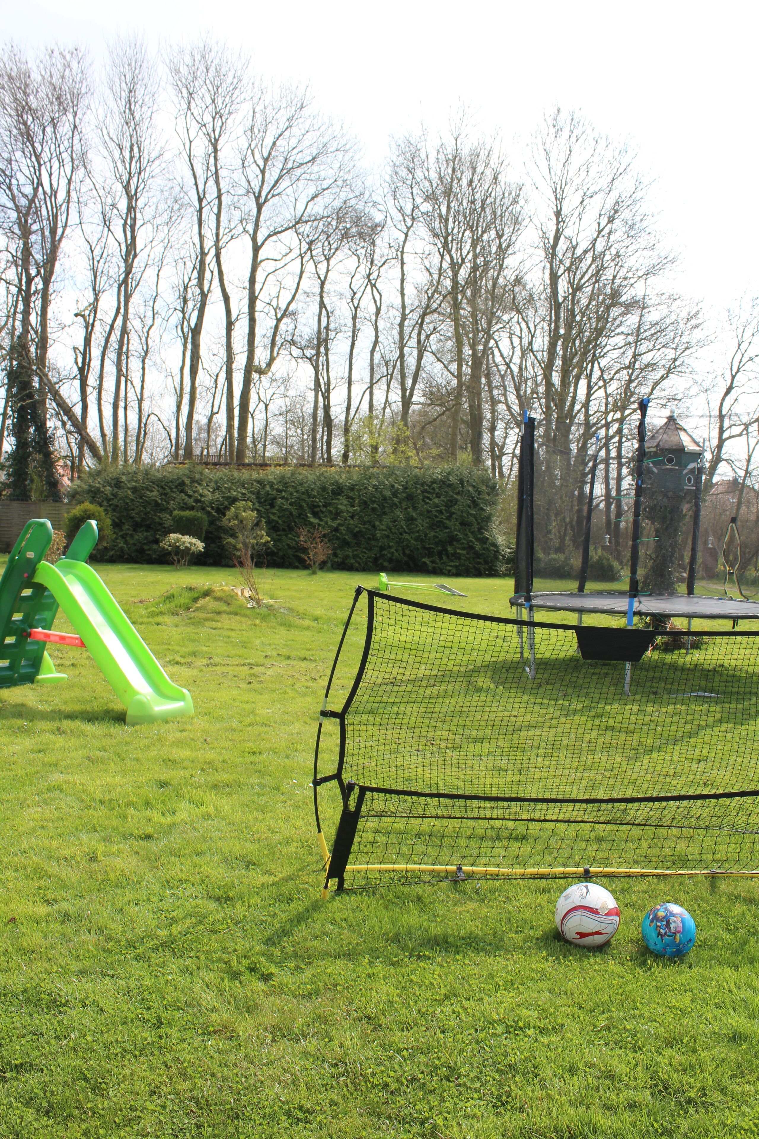A grassy area with a soccer goal, a slide, and two soccer balls.