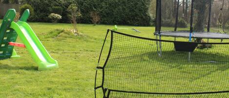 A grassy area with a soccer goal, a slide, and two soccer balls.