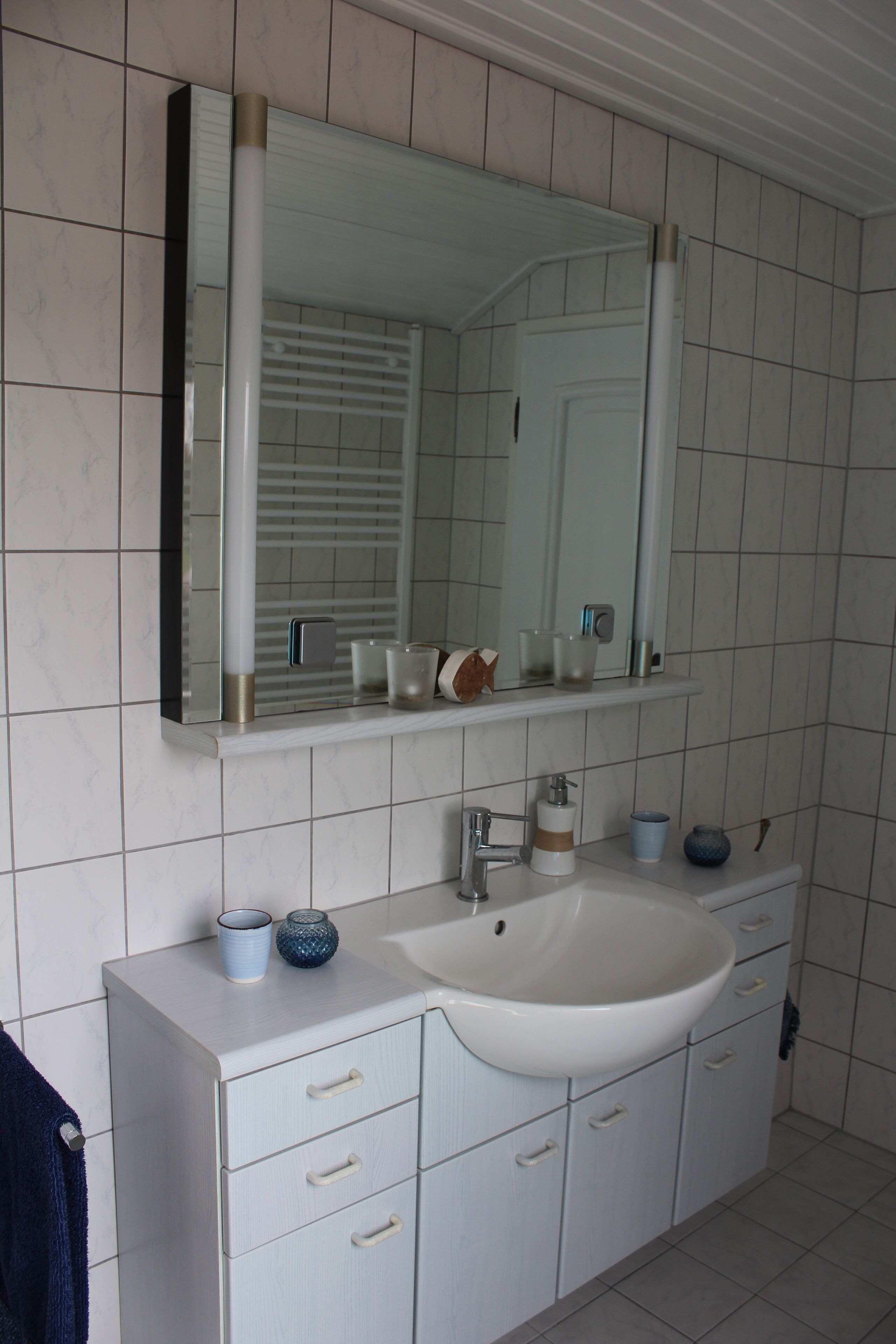 Une salle de bain avec un lavabo blanc, un miroir et des murs carrelés.