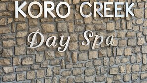 Un mur de pierres sur lequel est inscrit en grandes lettres blanches : « KORO CREEK Day Spa ».