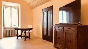 Um quarto com piso de madeira, uma mesa, um armário e uma televisão.