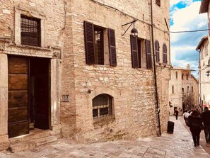 Una estrecha calle adoquinada con edificios históricos de piedra, puertas de madera y ventanas con contraventanas.