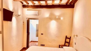 A bedroom with a wooden ceiling, a bed with white linens, a chair, and a wall-mounted TV. - Double Rooms Mavitur Rooms (Assisi)