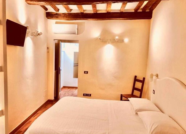 Un dormitorio con techo de madera, una cama con ropa blanca, una silla y un televisor montado en la pared.