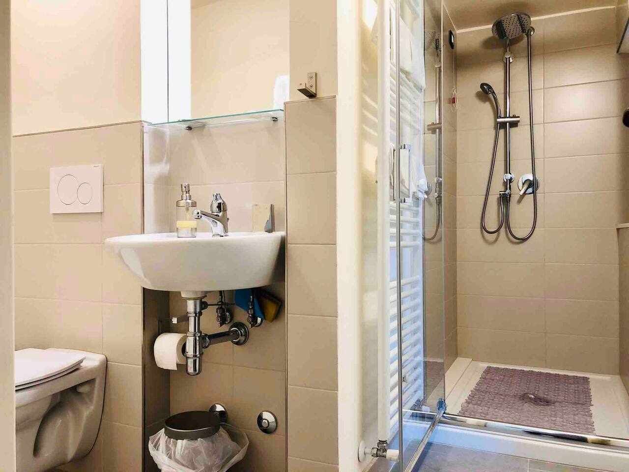 A bathroom with a glass shower enclosure, a sink with a mirror, and a toilet.