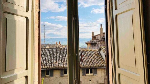 An open door with a view of a cityscape through a window, featuring traditional tiled roofs and buildings. - Double Room Mavitur Rooms (Assisi)