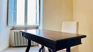 A room with a table and a chair, a window with open shutters, and a radiator. - Double Room Mavitur Rooms (Assisi)