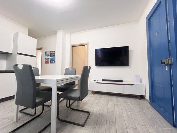 A modern room with a dining table, chairs, a flat-screen TV, and a blue door.