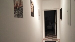 A hallway with a checkered floor, a black rug, and framed pictures on the walls.