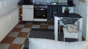 A compact kitchen with white cabinets, a stove, and a sink. There is a small table with a chair and a potted plant.