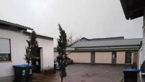 A courtyard with a small tree, two trash bins, and a building with a metal roof.
