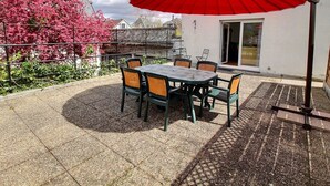 An outdoor patio with a table and chairs, a red umbrella, and a view of a building with a glass door. - Spacious Apartment with Terrace & Garage, 10 Min Walk to Park in Colmar (Colmar)