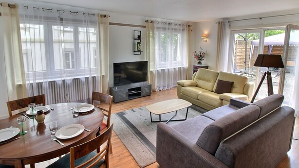 A living room with a sofa, TV, dining table set, and a lamp. - Spacious Apartment with Terrace & Garage, 10 Min Walk to Park in Colmar (Colmar)
