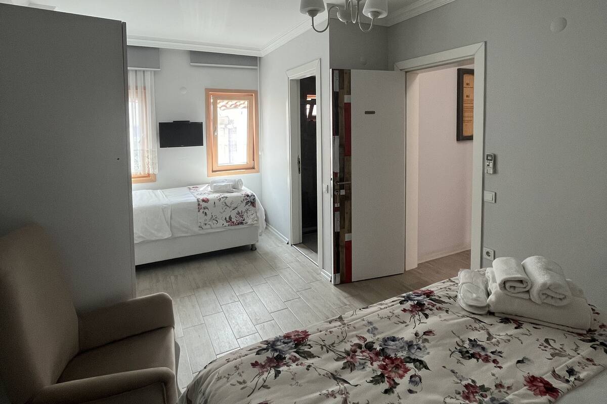 A bedroom with a bed, a chair, a wardrobe, and a door leading to another room.
