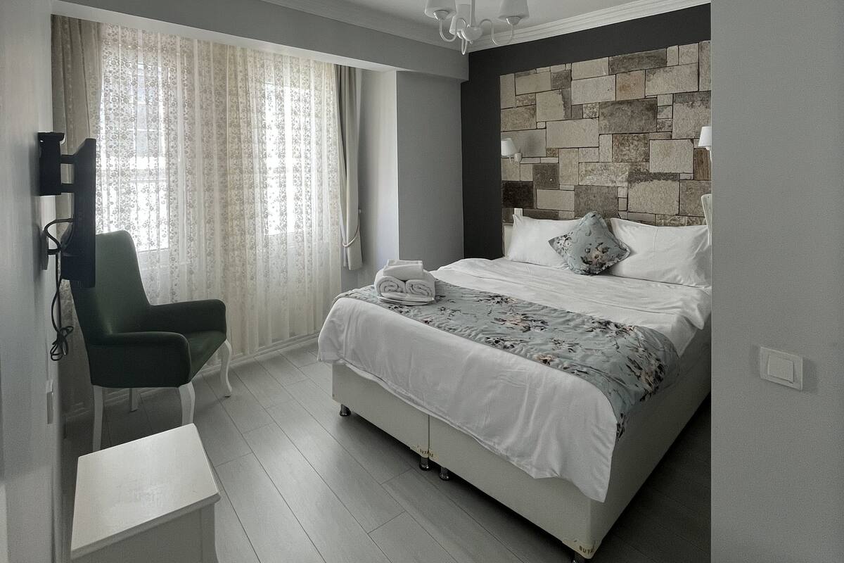 A bedroom with a bed, a chair, a desk, a television, and a window with curtains.