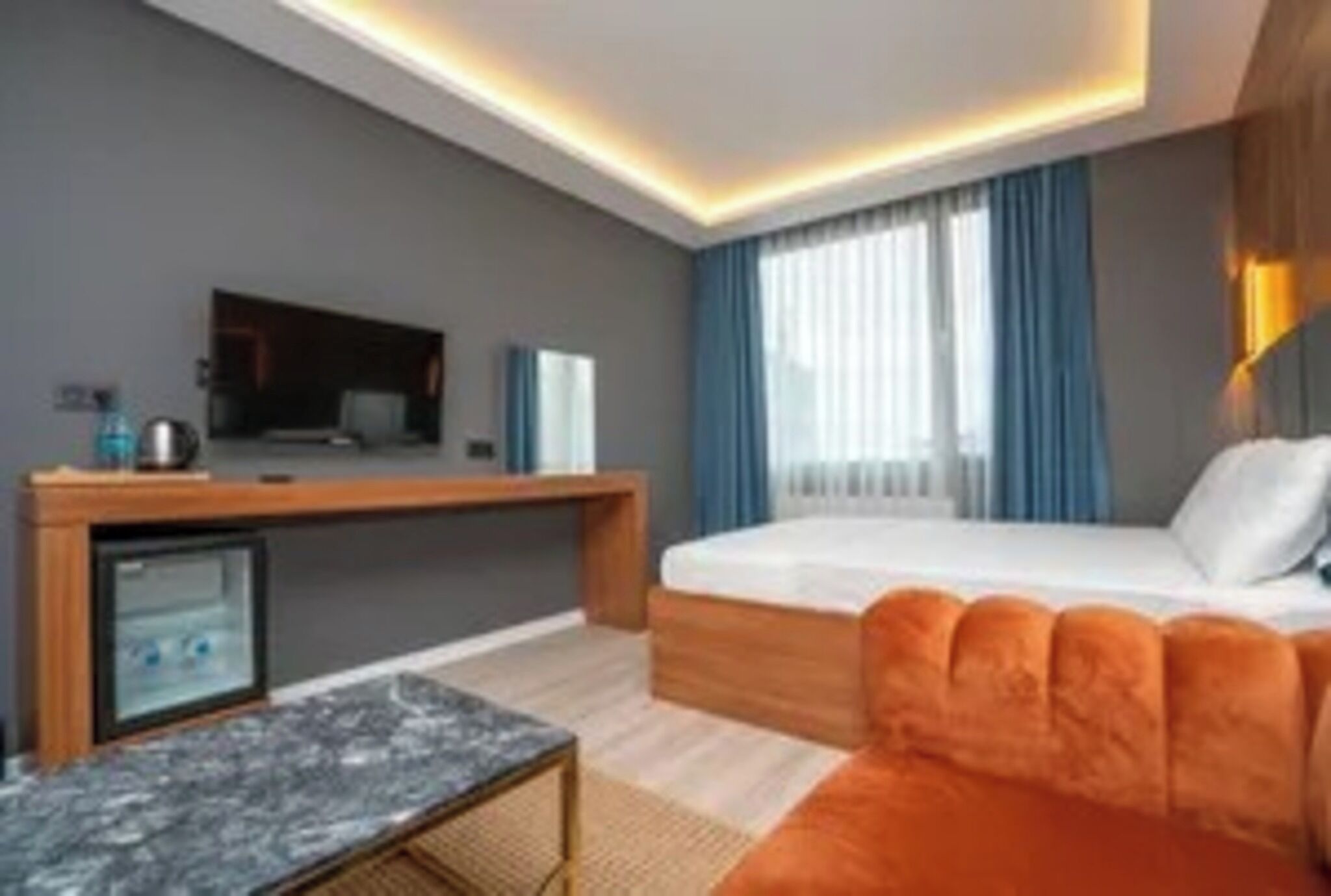 A modern hotel room with a bed, a desk, a television, and a small refrigerator.