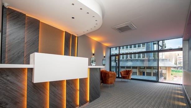 A modern reception area with a reception desk, two chairs, and a large window offering a view of the building's exterior. - Center Suite (Istanbul)