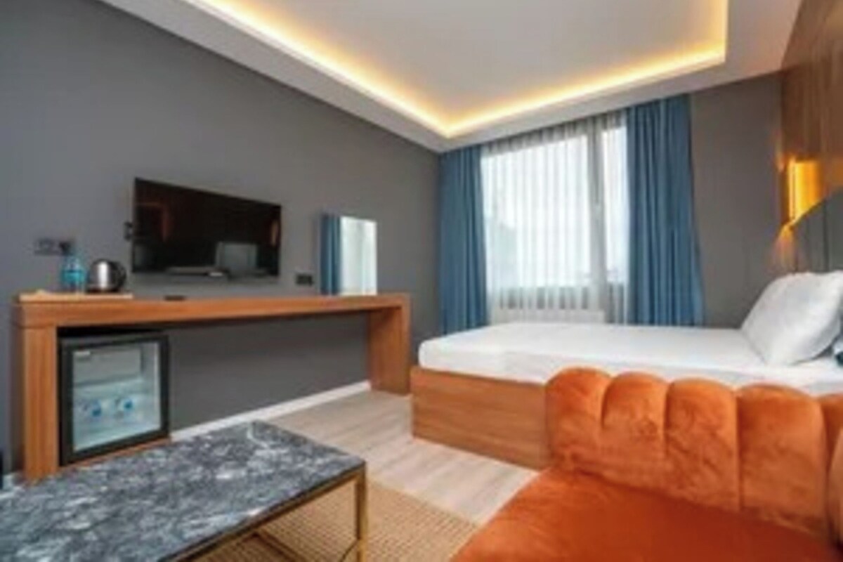 Una habitación de hotel moderna con una cama, un escritorio, un televisor y un refrigerador pequeño.