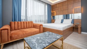 A modern hotel room with a sofa, a bed, a small table, and a wooden panel wall. - Center Suite (Istanbul)