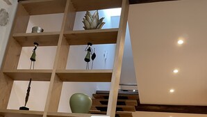 Un intérieur moderne avec un escalier en bois, un coin repas comprenant des chaises et une table, ainsi que des étagères ornées d’objets décoratifs.