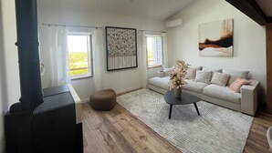 Un salon spacieux avec un haut plafond, une cheminée, un ensemble de canapés et une grande fenêtre donnant sur un paysage verdoyant.