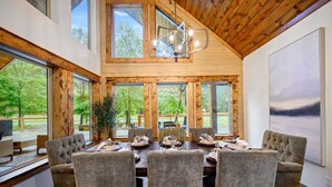 Zona pranzo con soffitto in legno, ampie finestre e un lampadario.
