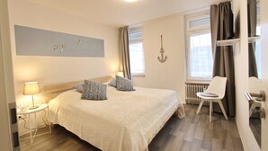 A bedroom with a bed, bedside table, lamp, chair, and a view of the outside. - Villa am Meer App. 5 incl. WLAN (Grömitz)