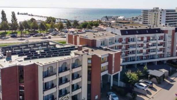 A multi-story hotel with a parking area and a view of the sea. - Villa am Meer App. 5 incl. WLAN (Grömitz)
