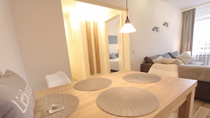 A modern living room with a wooden dining table, white chairs, a sofa, and a hanging light fixture. - Villa am Meer App. 5 incl. WLAN (Grömitz)