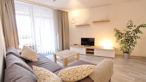 A modern living room with a sofa, a coffee table, a TV, and a potted plant. - Villa am Meer App. 5 incl. WLAN (Grömitz)