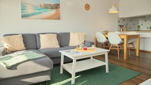 Una sala de estar con un sofá gris, una mesa de centro blanca y un cuadro de una playa.