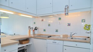 Una cocina moderna con armarios blancos, horno integrado, lavavajillas y un lavamanos con encimera de madera.
