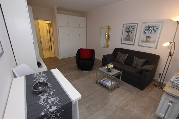 A living room with a sofa, a coffee table, a dining table with a bowl, a mirror, and framed pictures on the wall.