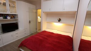 Une chambre à coucher avec un lit, un téléviseur et des meubles blancs avec des étagères.