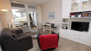 Un salon moderne avec un canapé, un fauteuil sur lequel est posée une serviette rouge, une table à manger et un téléviseur.