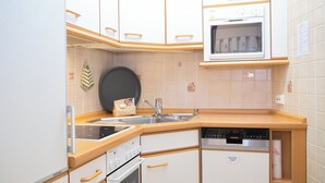 Uma cozinha compacta com armários brancos, forno embutido, micro-ondas e lava-louças.