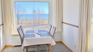 Uma sala de jantar com mesa posta para quatro pessoas, vista para o mar e janela com cortinas.