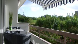A balcony with a wicker table and chairs, a vase of greenery, and a view of a garden. - House Baltic App. 40 incl. WLAN (Grömitz)