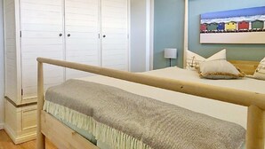 A bedroom with a bed, a wooden headboard, a nightstand, a lamp, a wardrobe, and a painting of colorful houses. - House Baltic App. 40 incl. WLAN (Grömitz)
