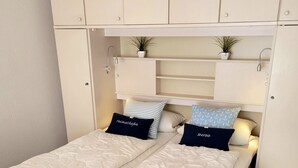 Un lit double avec deux oreillers, une tête de lit et une petite étagère avec des plantes.