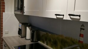 Een moderne keuken met witte kasten, een ingebouwde magnetron, een koffieapparaat en een fornuis.
